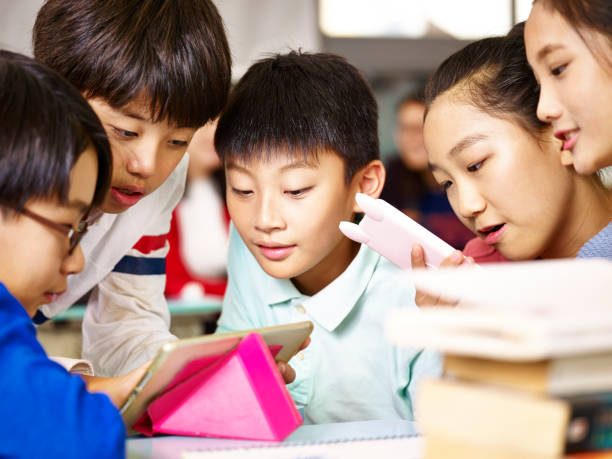 Five children gathered around tablets, looking at the screens and collaborating.
